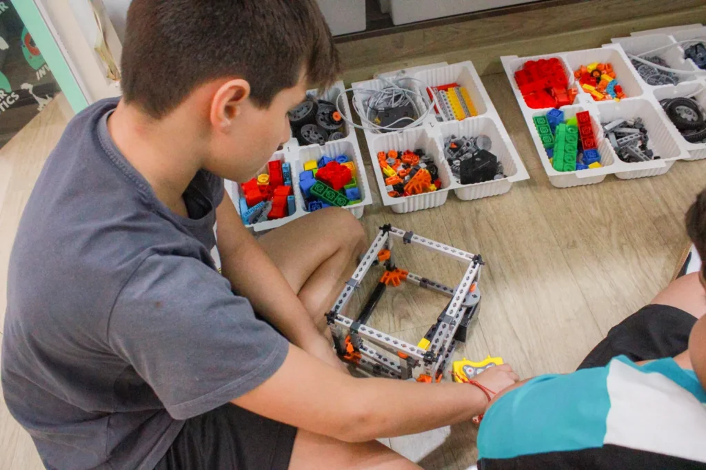 Aluno montando a estrutura de um robô com o kit individual ao lado