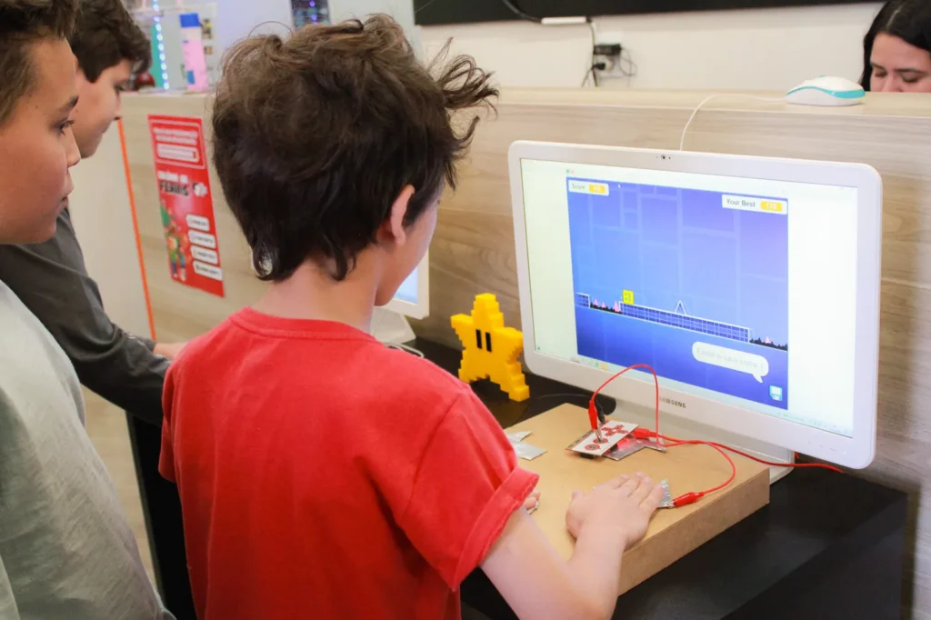 Aluno testando o próprio jogo com um controle maker que ele mesmo construiu em aula